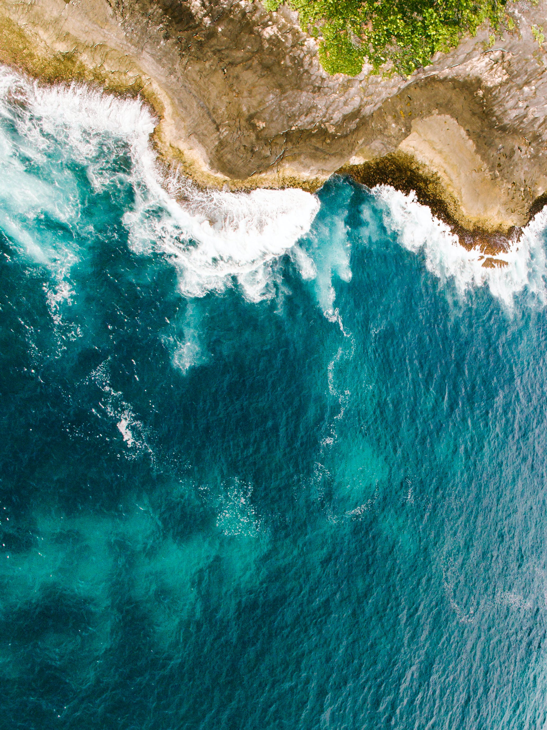 Image of a drone shot of a coastal cliff area with ocean waves crashing against cliff